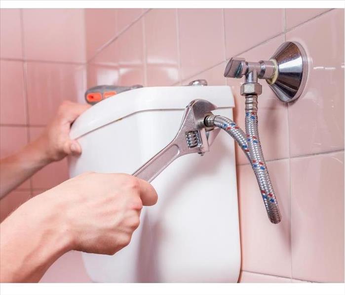 Plumber repairing a toilet pipe with a wrench